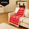 A red and white Christmas-themed blanket draped over a cream-colored sofa in a living room with a fireplace decorated for the holidays. Náhled obrázku produktu