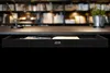 A black drawer is shown under a desk with a blurred background of bookshelves and plants. Podgląd zdjęcia produktu