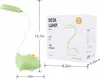 A green dinosaur-shaped desk lamp is shown next to its packaging box, with dimensions indicated. Produktbild-Vorschau