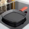 A square cast iron grill pan with an orange silicone handle cover rests on a black glass stovetop. Jars of dry goods are visible in the background. Náhľad obrázku produktu