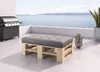 A pallet bench with a gray cushion sits on a patio overlooking the ocean, with a grill to the left and a plant to the right. Produktbild-Vorschau