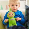 A young child is sitting on a couch, holding a green Teletubby plush toy. Voir les images du produit