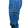 A close-up view of the side of blue denim work pants with multiple pockets and black accents. Náhled obrázku produktu