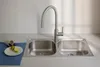 A stainless steel double sink with a modern faucet, placed on a countertop with a small plate of limes and a cup. Podgląd zdjęcia produktu