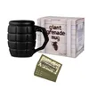 A black grenade-shaped mug and its packaging are displayed on a white background, with a stack of small cards in the foreground. Voir les images du produit