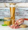 Three glass storage jars filled with pasta and small pasta shapes, arranged on a wooden surface with a distressed wooden background. Produktbild-Vorschau