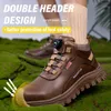 A pair of brown work boots with yellow toe protection, set against a mossy green background. Text overlays highlight features. Produktbild-Vorschau