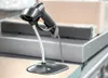 A barcode scanner on a stand is placed on a counter, with boxes in the background. Produktbild-Vorschau