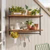 A two-tiered industrial-style wall shelf with various gardening items displayed on it, including plants, watering cans, and tools. Anteprima dell’immagine prodotto