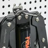 A close-up view of a black arm trainer attached to a white pegboard. Náhľad obrázku produktu