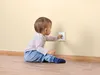 A baby is sitting on the floor and reaching for an electrical outlet. Náhľad obrázku produktu