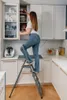 A woman is using a step ladder to reach into a kitchen cabinet. Voir les images du produit