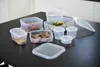 A collection of clear plastic food storage containers with lids, some filled with food, arranged on a dark surface. Produktbild-Vorschau