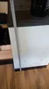 A close-up of a white stove with a measuring tape against it, on a wooden floor. Produktbild-Vorschau