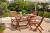 A wooden garden table and chairs set on a patio with plants and flowers in the background. Produktbild-Vorschau