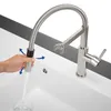 A hand is shown pulling down the flexible spout of a modern kitchen faucet over a sink. Anteprima dell’immagine prodotto