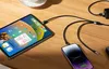 A tablet and a smartphone are charging on a wooden table using a multi-port charging cable. Produktbild-Vorschau
