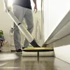 A person is using a cordless floor cleaner on a wooden floor next to a white wall. Produktbild-Vorschau