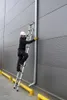 A person is using a ladder to access a gutter on the side of a building. Náhľad obrázku produktu