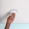 A hand is shown installing a smoke detector on a white ceiling. Náhľad obrázku produktu