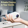 A hand holding a white mini-projector over a table with a magazine. Produktbild-Vorschau