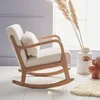 A cream-colored boucle fabric rocking chair with a wooden frame is placed on a white wooden floor next to a window. Dried pampas grass in a vase and a terracotta vase with dried flowers are also visible. Anteprima dell’immagine prodotto