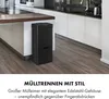 A black sensor trash can with multiple compartments is placed in a modern kitchen next to a kitchen island. Produktbild-Vorschau