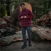A man stands in a forest setting with large logs behind him. Náhľad obrázku produktu