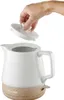 A hand is shown placing the lid on a white ceramic kettle with a wooden base. Produktbild-Vorschau