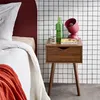 A bedside table with a lamp, books, and a glass of water next to a bed. Produktbild-Vorschau