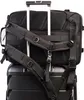 The back of a black backpack is shown attached to the handle of a black rolling suitcase. Náhled obrázku produktu