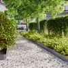 A garden path made of white gravel, bordered by green bushes and trees, with a fence in the background. Produktbild-Vorschau