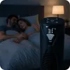 A couple sleeps peacefully in bed at night, while a black tower fan stands in the foreground, displaying temperature and fan speed. Podgląd zdjęcia produktu
