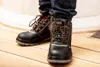 A person wearing dark blue jeans and black work boots with orange laces stands on a wooden floor. Náhľad obrázku produktu