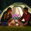 A couple sitting in front of a tent at night, with a solar-powered flower light in between them. Náhled obrázku produktu