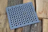 A square metal grate with many circular holes rests on a pile of logs. Voir les images du produit