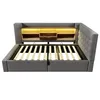 A grey upholstered bed frame with a wooden headboard featuring built-in lighting and storage compartments. Produktbild-Vorschau