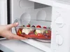 A hand is placing a glass baking dish filled with food into a microwave. Anteprima dell’immagine prodotto