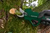 A hand wearing a glove is using an electric pruning shear to cut a branch off a tree covered in moss. Produktbild-Vorschau