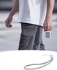 A person walking outdoors, holding a small square device with a wrist strap attached. Produktbild-Vorschau