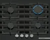 A top-down view of a black gas cooktop with four burners, two of which are lit with blue flames. Anteprima dell’immagine prodotto