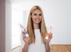 A woman is holding two tubes of paint in front of a bright, modern room with large windows. Produktbild-Vorschau