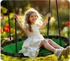 A young girl is happily swinging on a large, round swing in a garden setting. Podgląd zdjęcia produktu