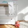 A close-up of a white dresser with a white muslin cloth draped over the top, and a pink stuffed fox toy on the floor next to it. Sunlight casts shadows on the wall. Produktbild-Vorschau