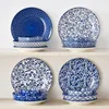 Four sets of blue and white patterned ceramic plates and bowls are displayed on white shelves. Produktbild-Vorschau