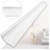 A white decorative molding strip is shown diagonally against a light gray and white background. A small side table with a vase and flowers, and a portion of a white sofa are visible in the background. Anteprima dell’immagine prodotto