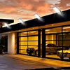 Four LED solar lights mounted on the roof of a modern garage with a glass door, showcasing cars inside. The sky is a dramatic sunset. Produktbild-Vorschau