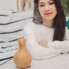 A woman is sitting at a table with a humidifier in front of her, which is emitting a mist. Produktbild-Vorschau