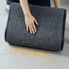 A hand is shown touching a grey striped doormat on a tiled floor, with some dirt scattered around. Podgląd zdjęcia produktu
