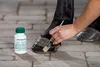 A person is applying a hoof product to a horse's hoof with a brush. A bottle of the product is visible next to the hoof. Produktbild-Vorschau